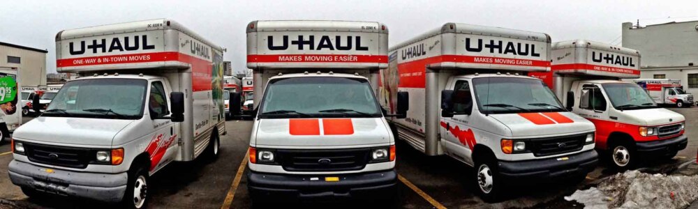 A row of UHaul moving trucks in a parking lot outside a rental location on a winter day.